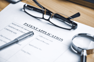 USPTO patent application form with magnifying glass representing the filing process and costs involved in obtaining a U.S. patent
