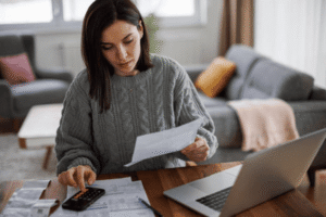 Small business owner calculating financial benefits and cost savings from trademark registration using calculator and documents at home