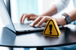Yellow caution warning sign next to laptop alerting startup founders about critical IP mistakes that reduce valuation during investment and acquisition